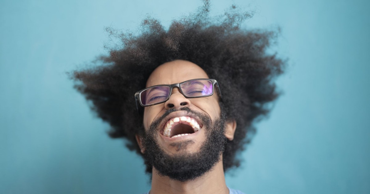 Close-up of a happy man with glasses and wild hair laughing against a blue background.