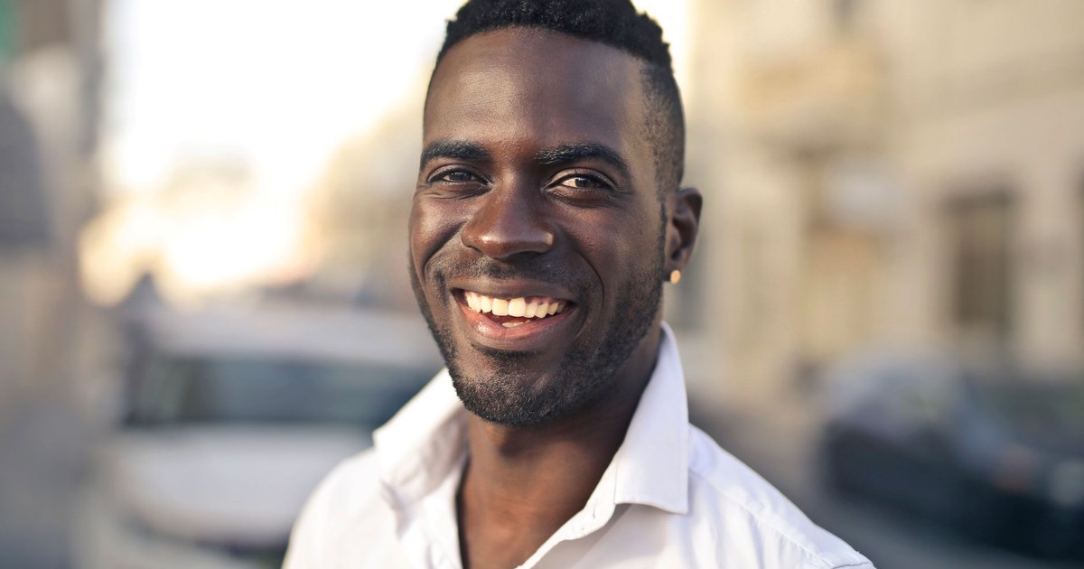 Portrait of a smiling man in a white shirt standing outdoors on a sunny day.