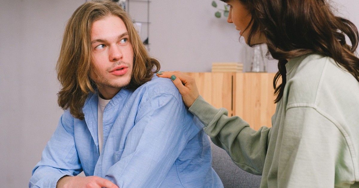 Concentrated woman talking and touching shoulder of pensive male in light room in daytime