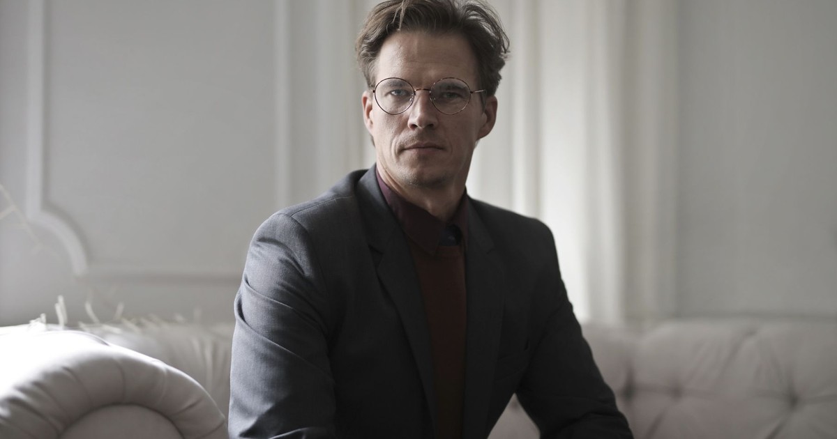 Confident mature male entrepreneur wearing classy suit sitting on comfortable couch in luxury living room and looking at camera