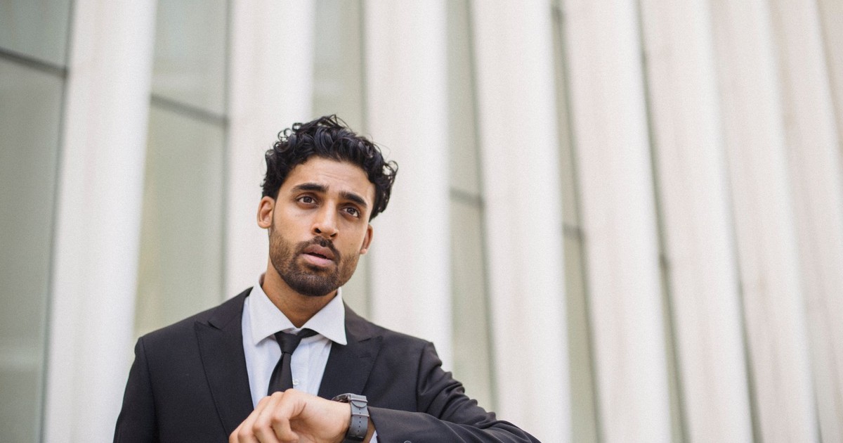 A professional man in a suit checks the time on his watch while standing outside, capturing a business theme.