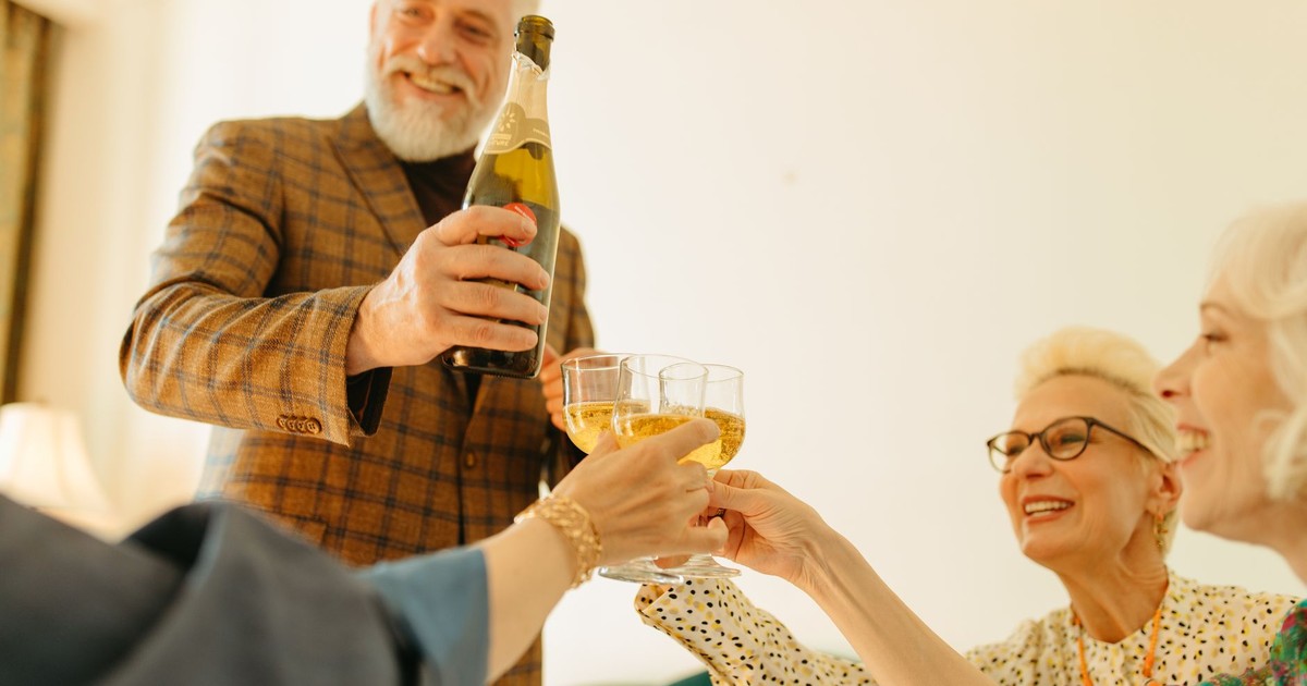 A group of senior friends enjoying a champagne toast together indoors, celebrating with smiles and glasses clinking.