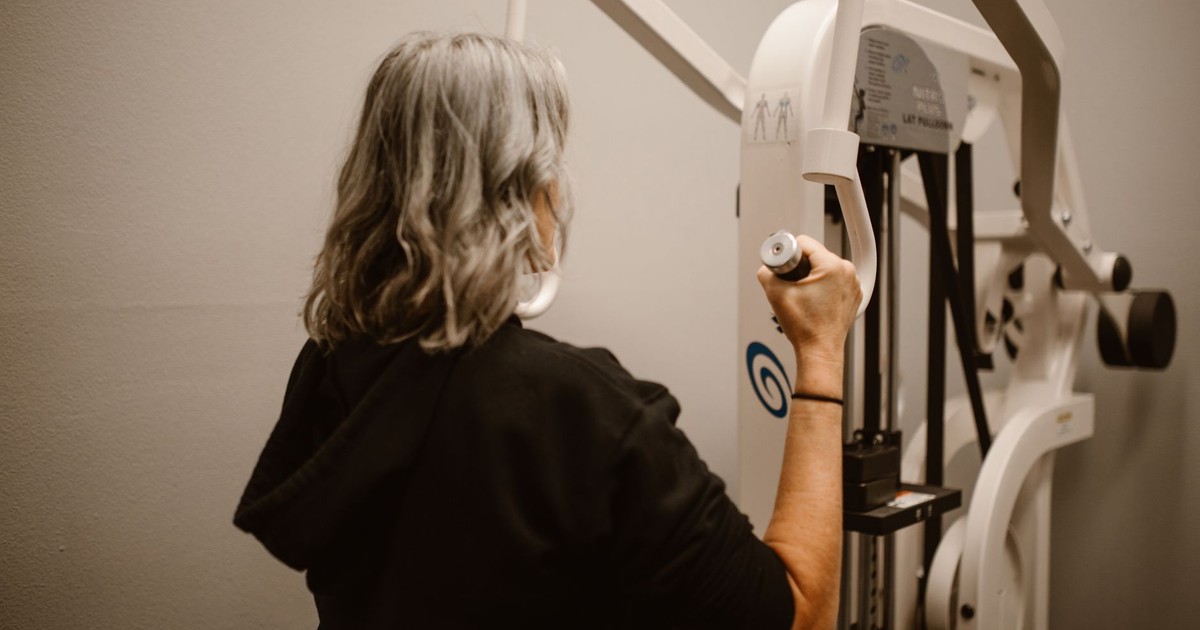 A senior woman uses the lat pulldown machine in a gym for strength training.