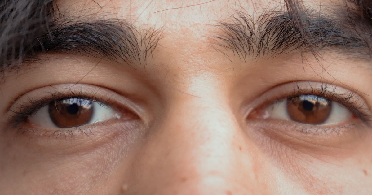 Closeup of crop calm ethnic person with thick eyebrows and brown eyes looking at camera