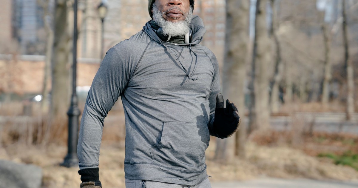 Elderly man exercising outdoors in winter, wearing gray sweater and beanie.