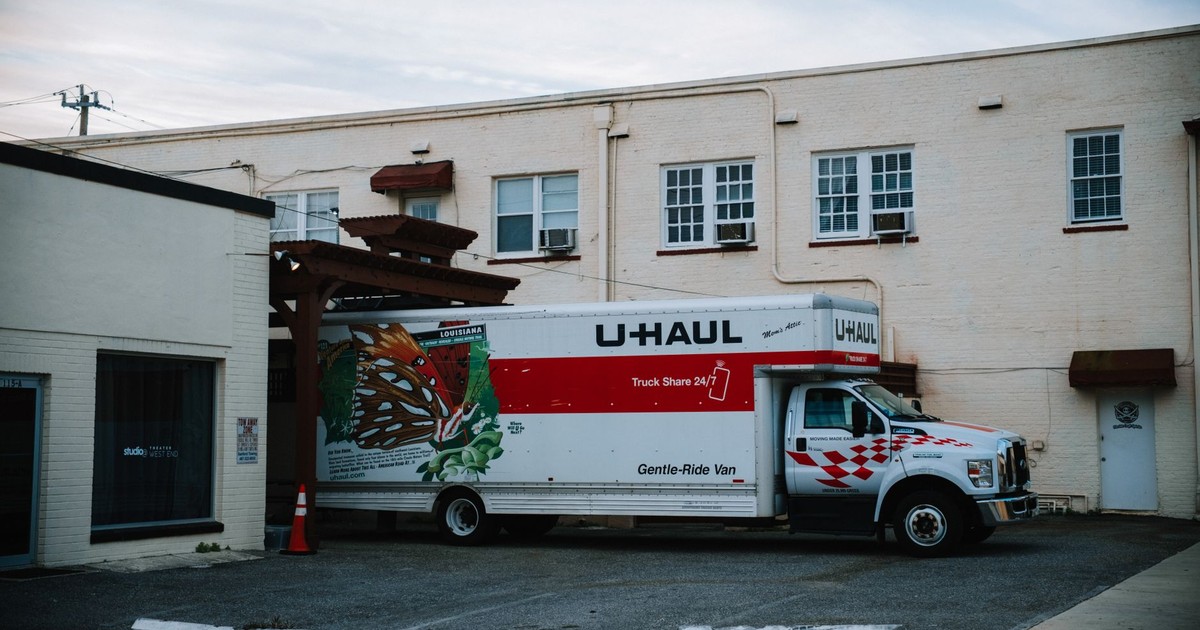 A U-Haul moving truck parked in front of a beige warehouse building.