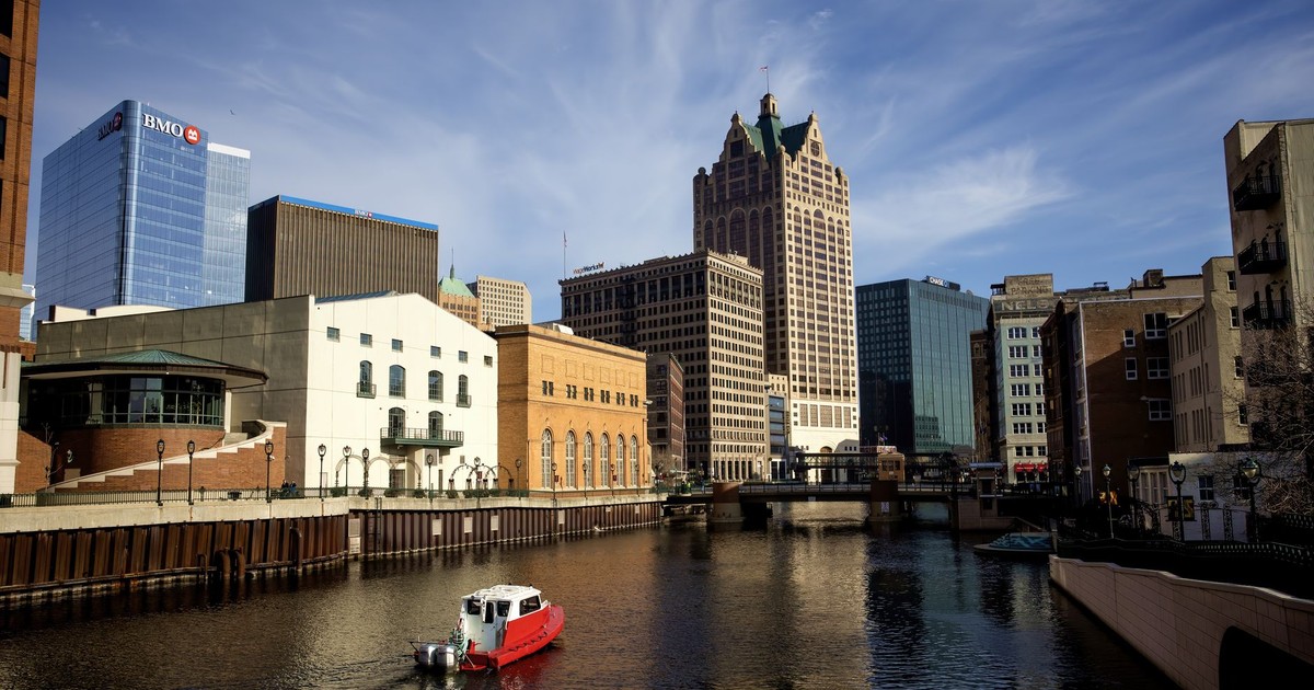 Panoramic view of Milwaukee River with iconic city buildings and a boat.