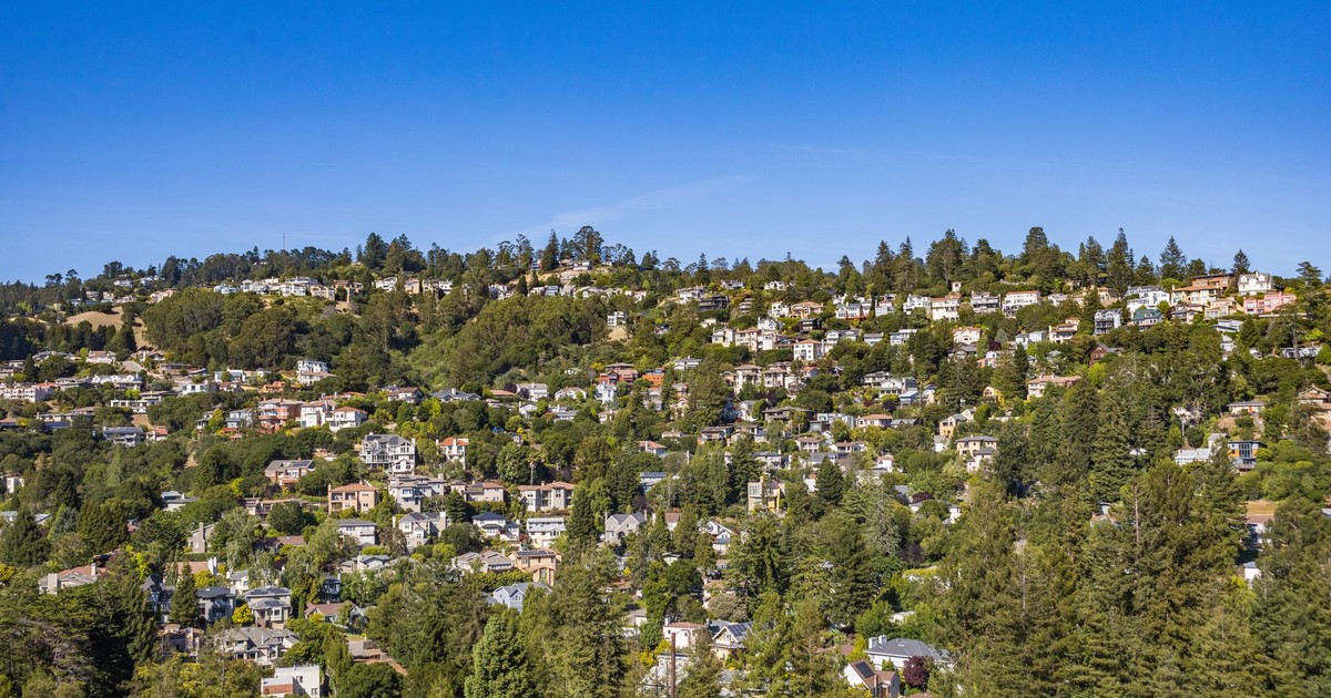A scenic aerial view of a lush residential area on a hillside under clear blue skies.