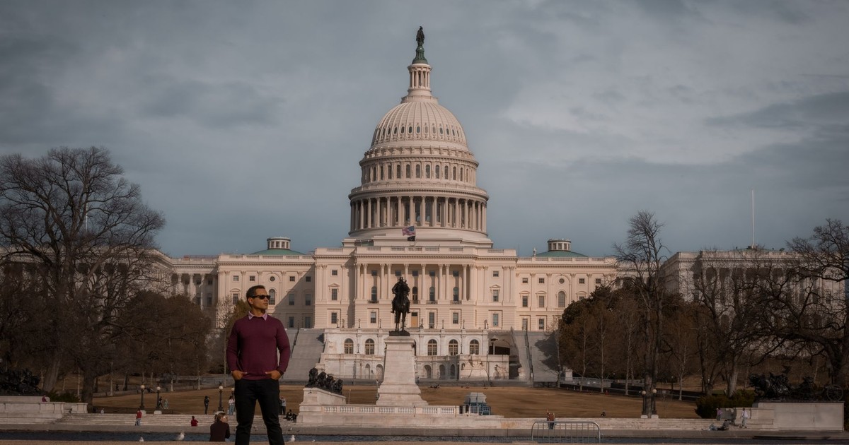Person standing in front of the iconic United States Capitol on a clear day.