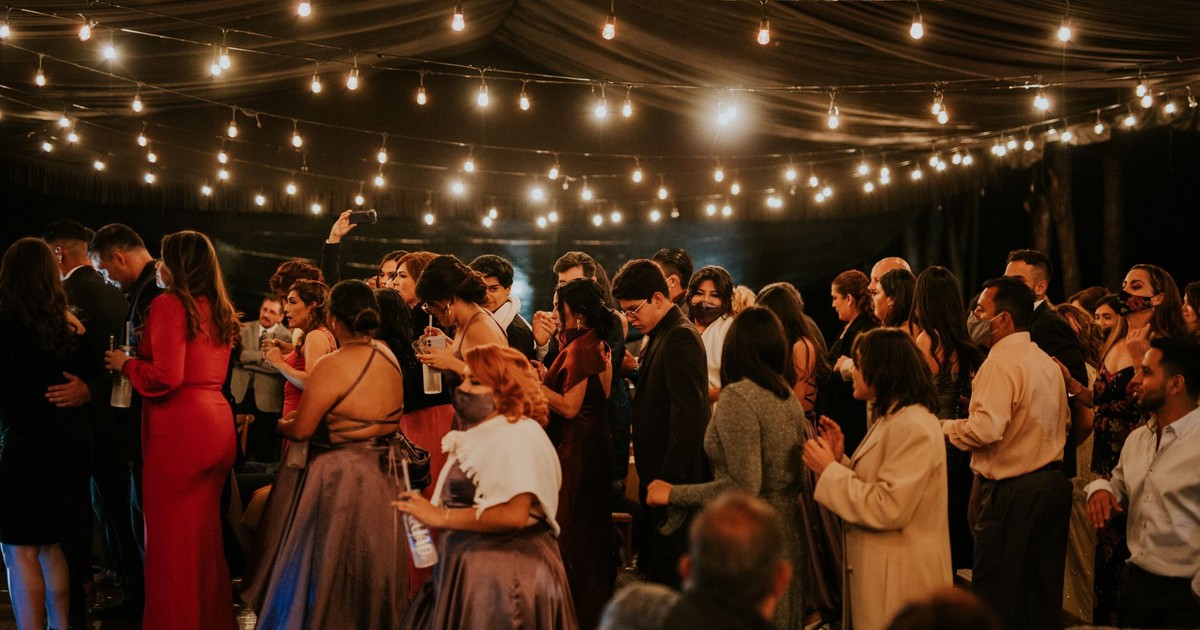 A joyful indoor wedding celebration with elegantly dressed guests under twinkling string lights.