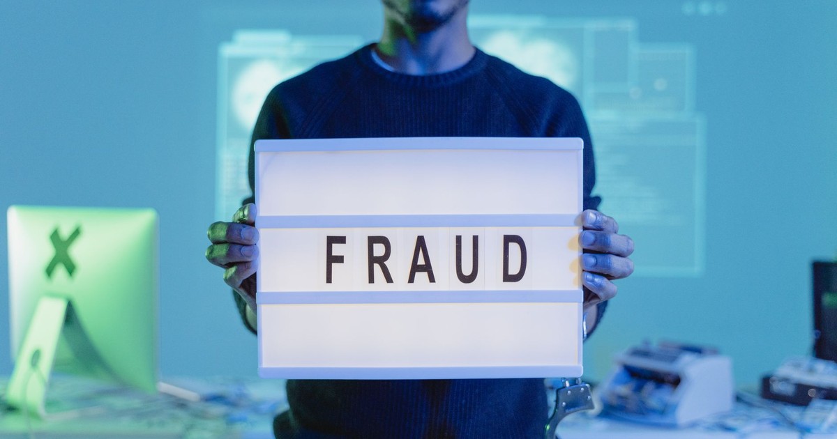 A man holding a sign reading 'FRAUD' in a tech environment, highlighting cybersecurity concerns.