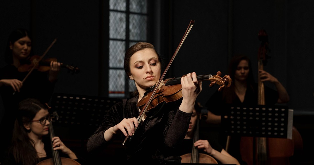 A female violinist plays passionately in a classical orchestra setting.
