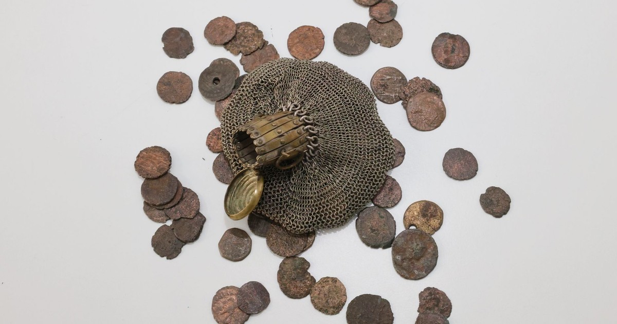 Top-down view of ancient coins scattered with a historical chainmail glove on a white surface.