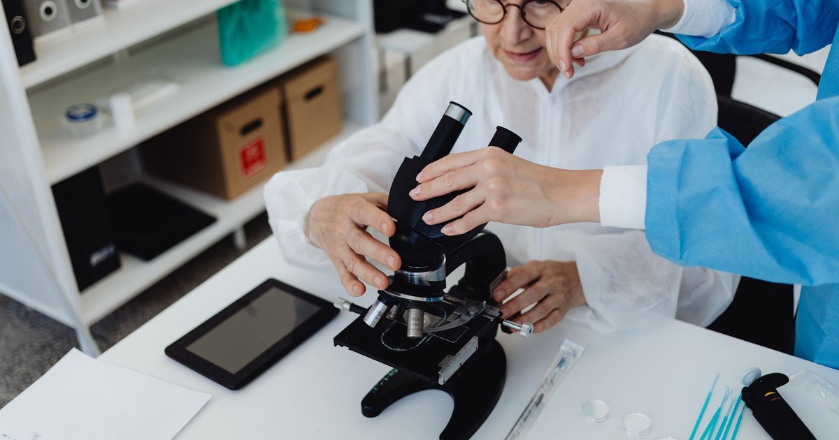 Senior scientist using a microscope with assistance in a laboratory setting, demonstrating research and analysis.