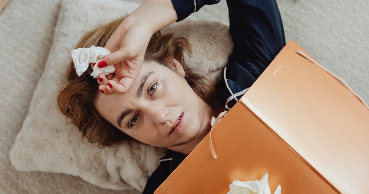 A woman lies on a pillow, holding crumpled tissues, conveying a sense of sadness or exhaustion.