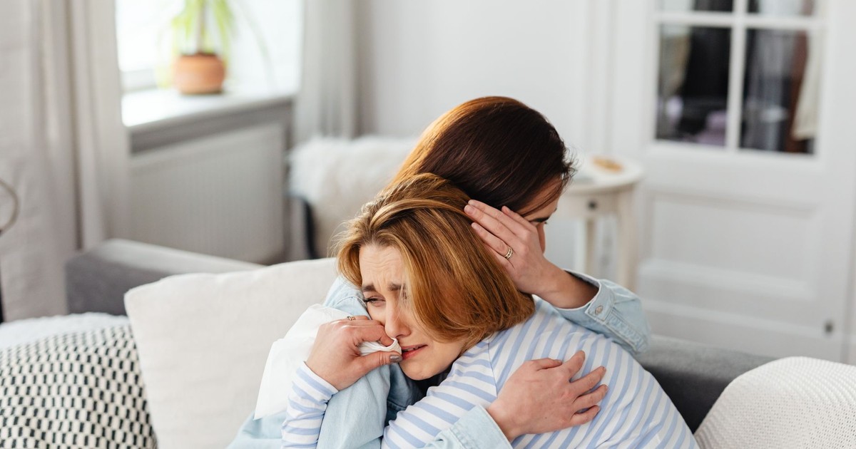 Two women embrace on a couch, conveying emotions of comfort and support indoors.