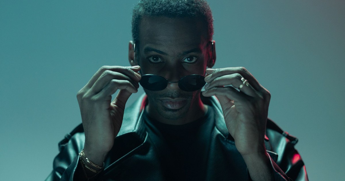 Man in a leather jacket adjusting sunglasses in a conceptual cyberpunk setting.