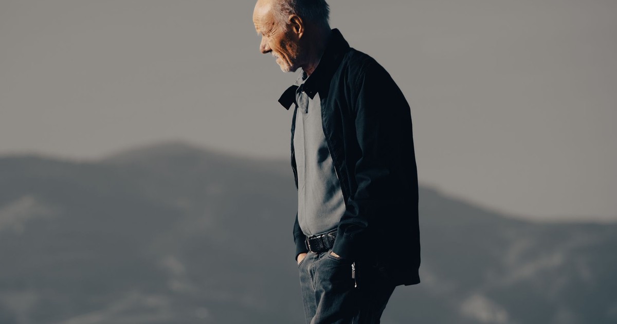 Senior man walking with hands in pockets against mountain backdrop during the day.
