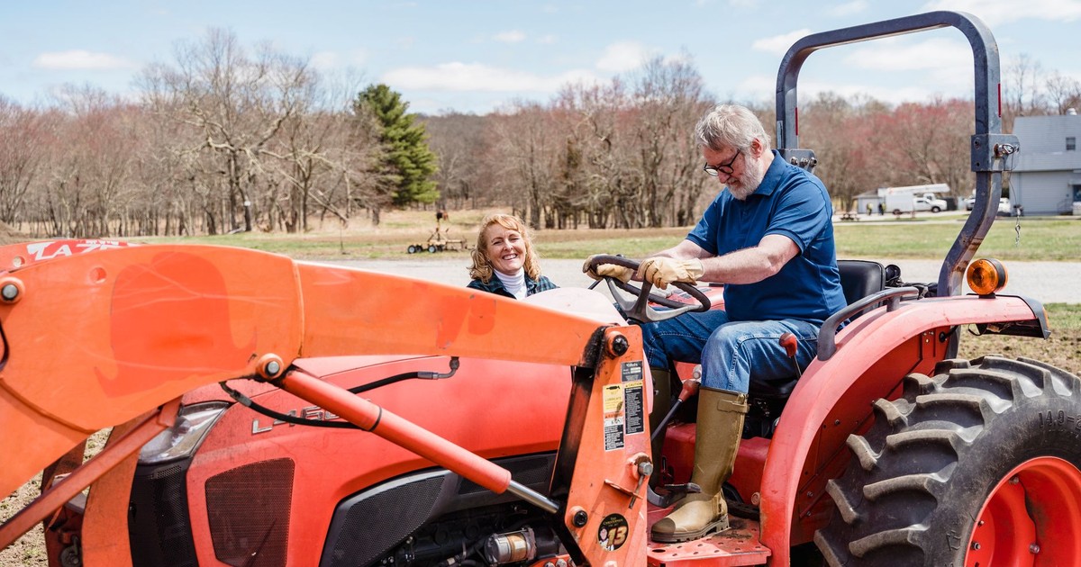Senior couple sharing a joyful moment on a tractor ride in a countryside farm setting.