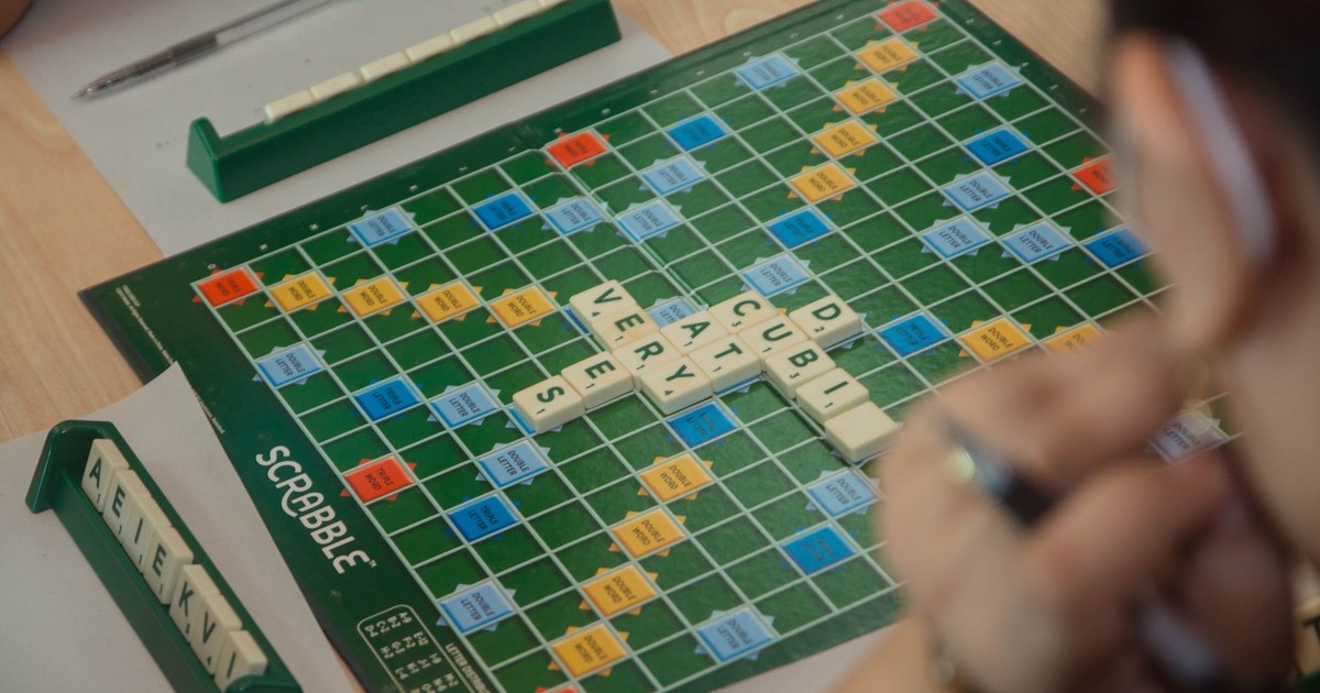 Players engaged in a strategic Scrabble game indoors on a wooden table.