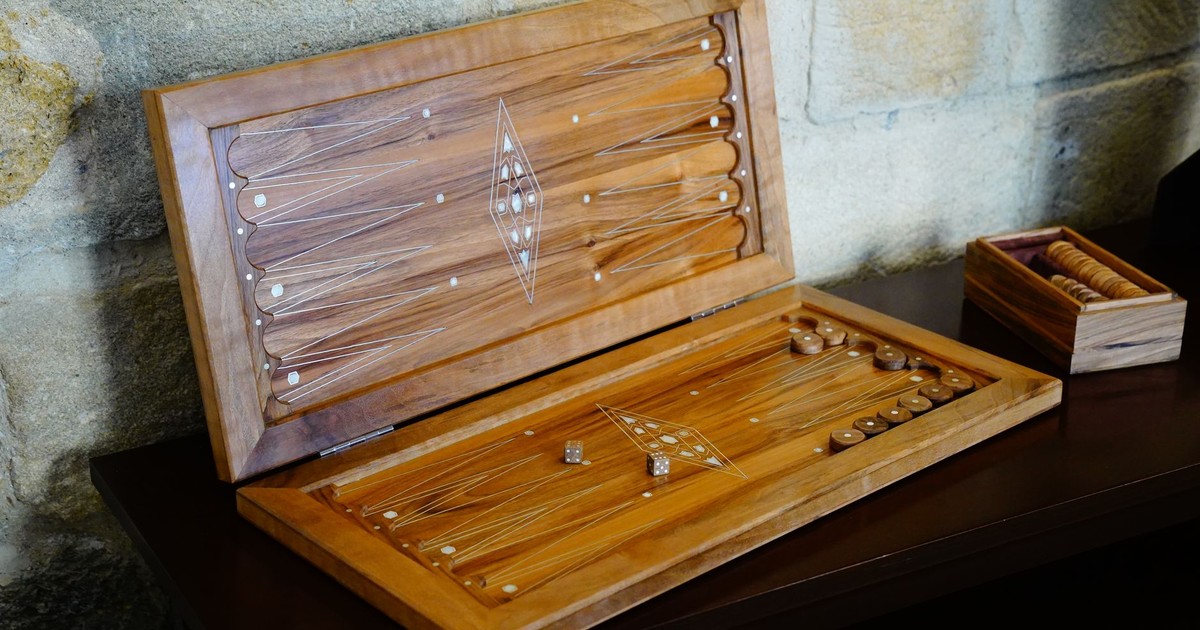 Elegant wooden backgammon set open on a rustic table with stone wall background.