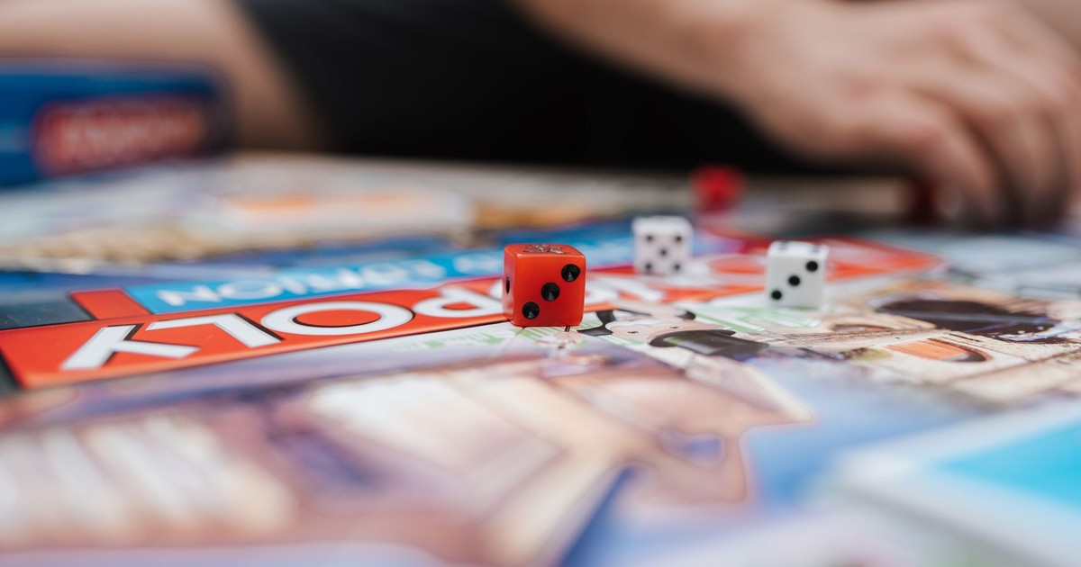 Crop anonymous person sitting at desk with game board and dices while playing Monopoly