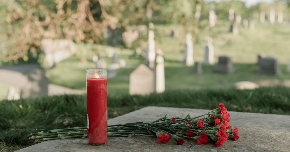 A serene cemetery scene with a red candle and carnations honoring a memory.