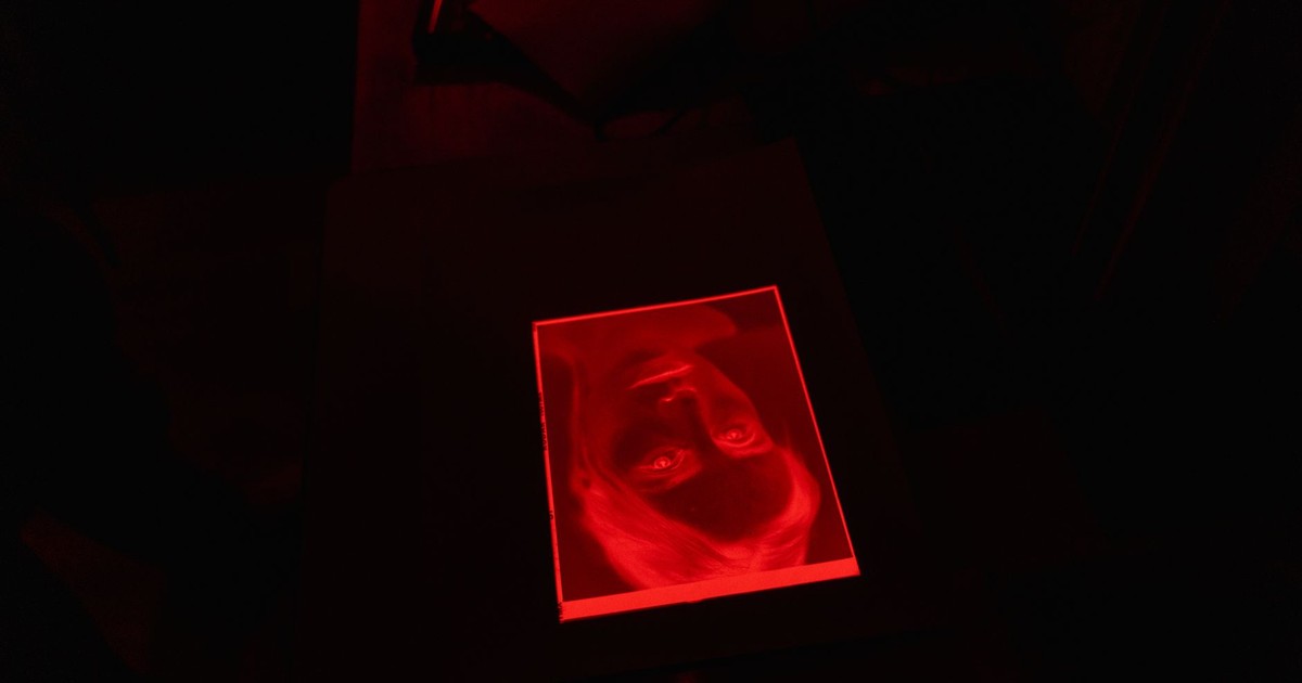 A red-tinted photograph lies on a black surface in a dark room, creating a mysterious ambiance.