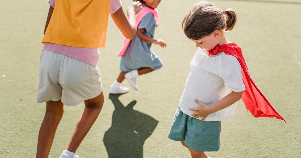 Children dressed as superheroes playing and running outdoors on a sunny day.