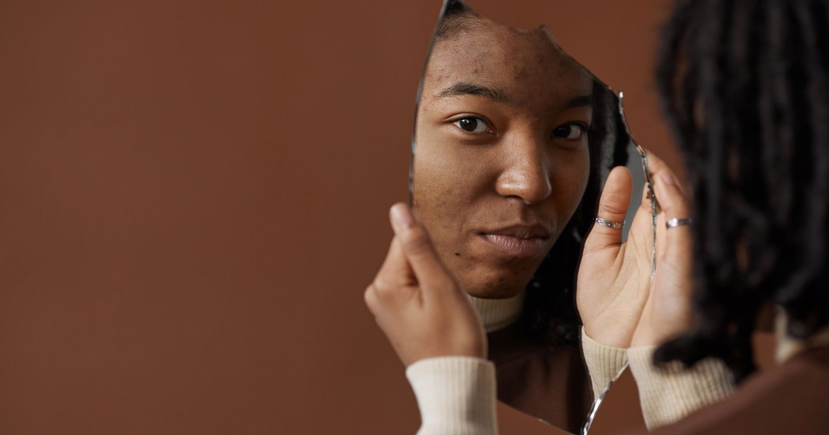 A woman holding and looking into a broken mirror, reflecting on self image and identity.
