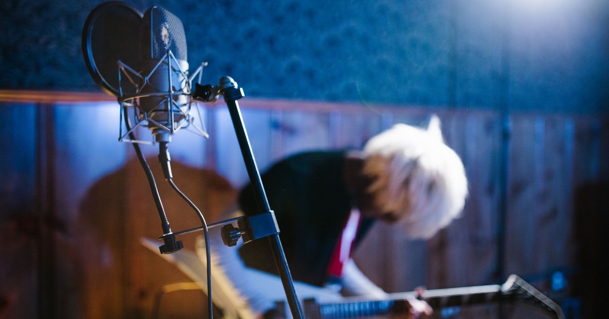 Blurred guitarist in a vibrant studio, mic in foreground capturing dynamic energy.