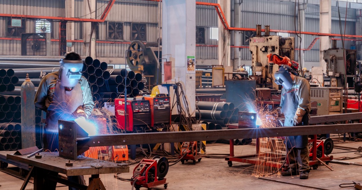 Two welders wearing protective gear working in a busy industrial factory workshop.