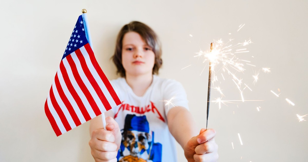 Young child joyfully holding American flag and sparkler indoors, celebrating USA holidays.