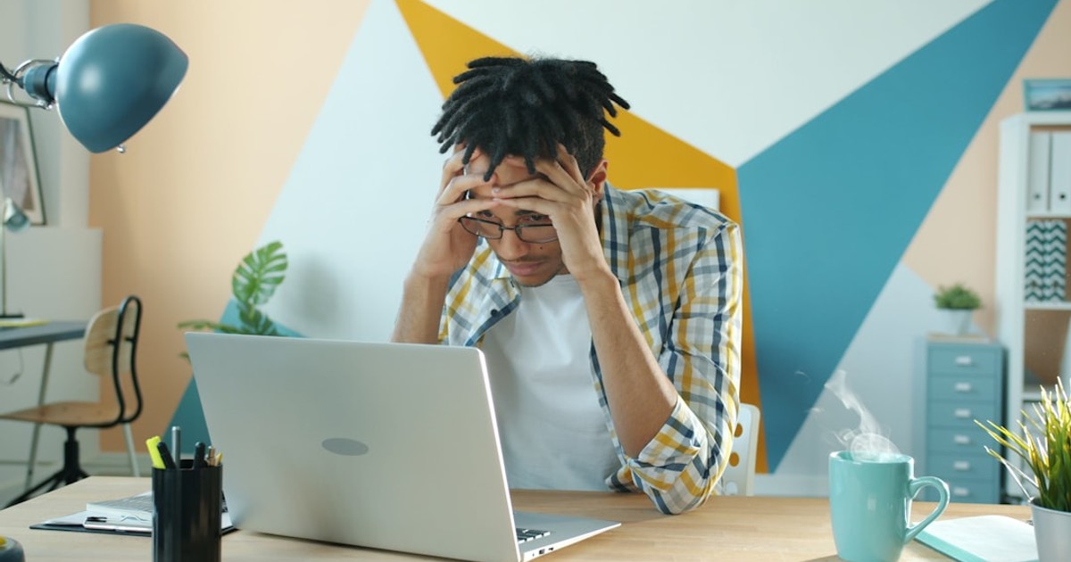 Man holding head in frustration at desk with laptop.