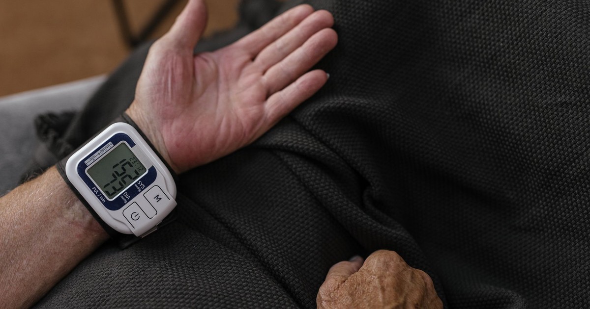 A senior adult using a wrist blood pressure monitor at home, focusing on health management.
