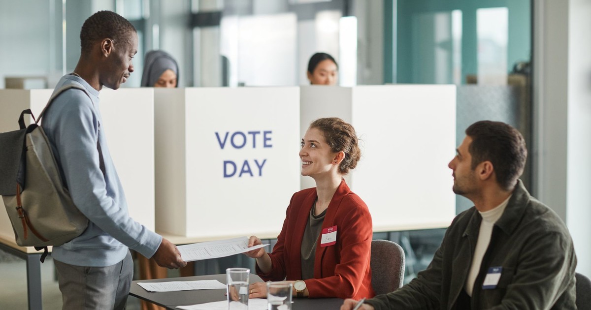 Diverse group of voters and officials at an indoor polling station on voting day.