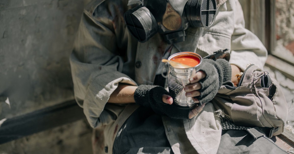 A person wearing a gas mask holding canned tomato soup, symbolizing survival.