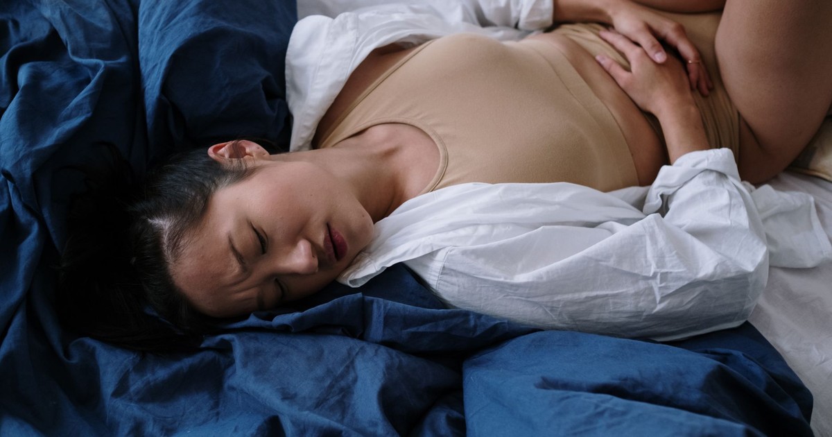 A woman lying on a bed in discomfort due to stomach pain, expressing symptoms of illness.