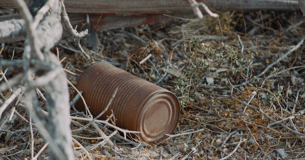 A rusty can lies amidst dry grass and branches in Joshua Tree, CA, capturing decay and desert beauty.