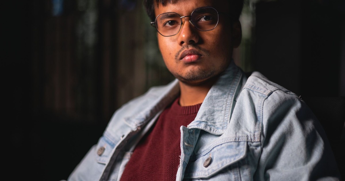 Portrait of a man with eyeglasses and denim jacket, exuding a serious demeanor.