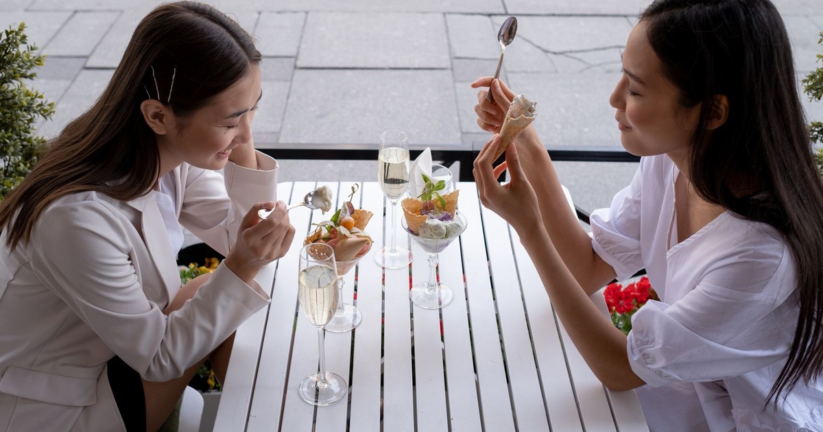 Two women sharing ice cream and champagne outdoors, enjoying a joyful dining experience.