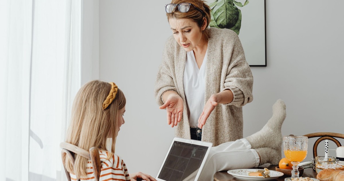 A mother scolds her teenage daughter absorbed in her laptop during breakfast at home.