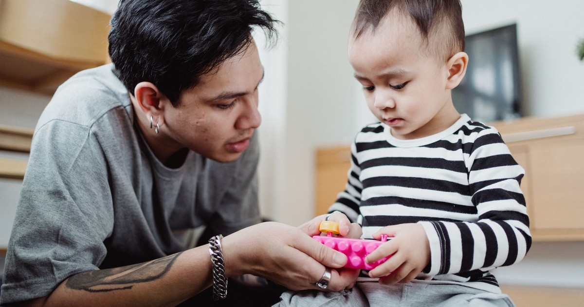 A father and son enjoy quality time together indoors, playing with colorful toys.