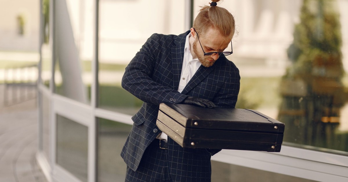 Businessman with a briefcase examines documents outside a modern building in the daytime.