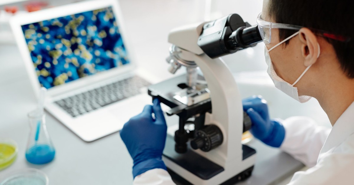 Scientist examining samples under a microscope in a lab with laptop display.