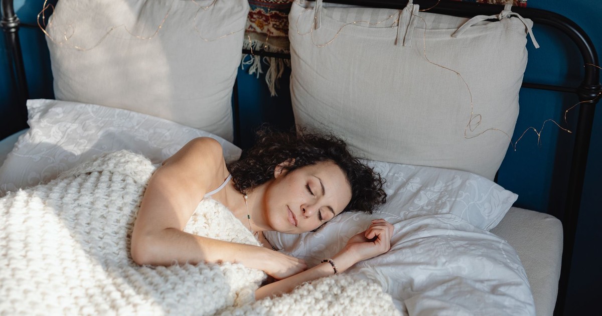 A young woman with curly hair sleeping peacefully in a cozy bed with knitted blankets.