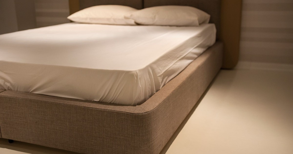A close-up view of a minimalist bedroom featuring a bed with white linen sheets and plush pillows.