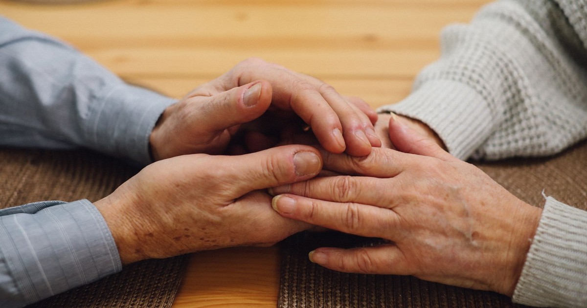 A close-up of an elderly couple holding hands on a wooden table, signifying love and companionship.