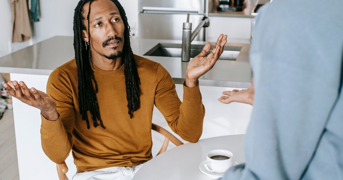 Black male sitting at table and arguing with standing near table female in casual outfit in light kitchen