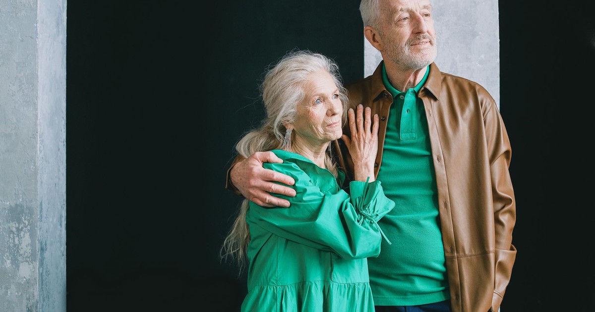 An elderly couple standing and embracing, clad in earthy tones, conveying love and togetherness.